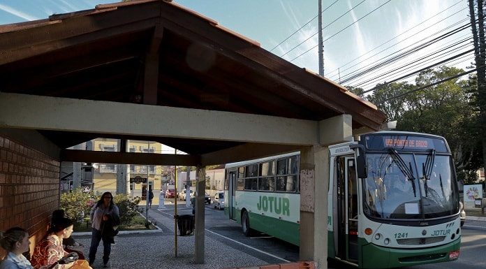 ônibus da jotur parado em frente a um ponto de ônibus de tijolos a vista em uma praça
