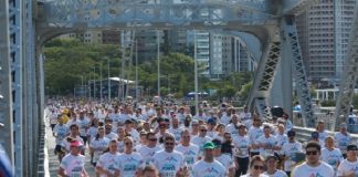 centenas de pessoas com mesma camiseta correndo sobre a pista da hercílio luz