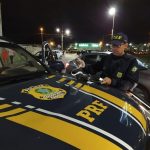 agente da prf confere resultado de teste de alcoolemia sob capô da viatura