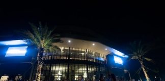 fachada iluminada da arena petry com dezenas de pessoas na frente em foto noturna