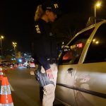 agente feminina da prf usa o bafômetro passivo com sinal vermelho em um motorista que não aparece, dentro de um carro visto de lado