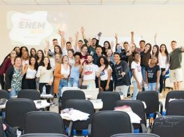 alunos e alunas em pé na frente da sala posam animados para a foto