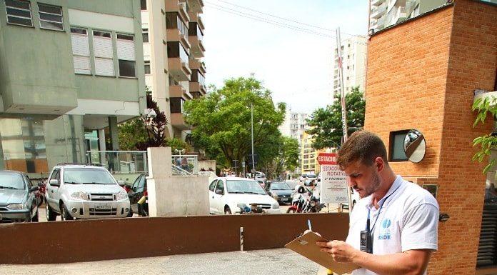 fiscal anota em prancheta em pé ao lado de bueiros abertos em área de estacionamento; ao fundo o hospital celso ramos