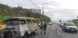 kombi totalmente destruída pelo fogo com homens e cones em volta, carros passando ao lado