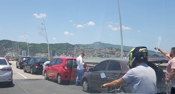 quatro veículos parados em linha na ponte e pessoas em volta