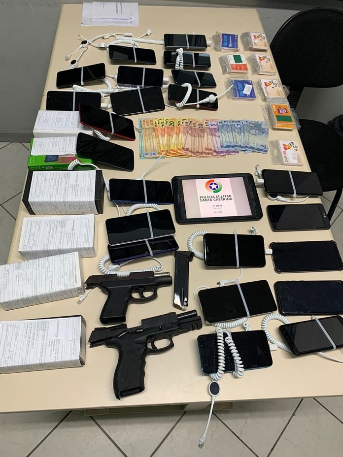mesa com duas armas, aparelhos celulares e tablet com logo da pmsc