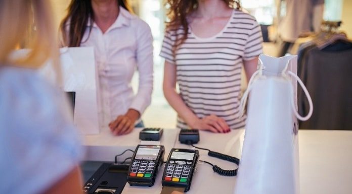 duas mulheres em frente a um balção de loja com duas máquina de cartão e mulher do outro lado do balcão