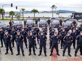 agentes da guarda alinhados em sentido com viaturas ao fundo estacionadas ordenadas em volta, na frente da prefeitura