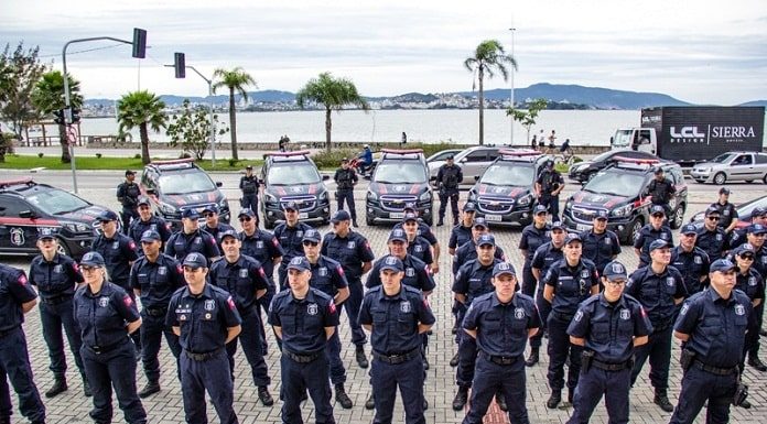 agentes da guarda alinhados em sentido com viaturas ao fundo estacionadas ordenadas em volta, na frente da prefeitura