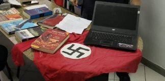 sobre uma mesa de mármore estão diversos livros do nazismo, camiseta com suástica e notebook