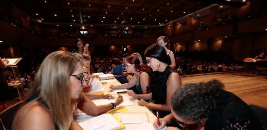 mesa onde mulheres estão dos dois lados, uma assinando papeis, outras entregando