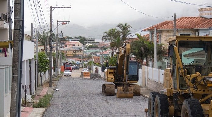 retroescavadeira e máquina de terraplanagem estacionadas em rua com cobertura de britas, em obras