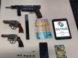armas, celular e balas dispostas sobre uma mesa com tablet com logo da pmsc