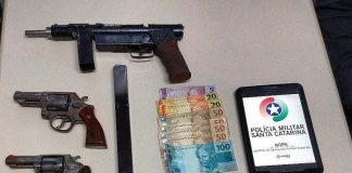 armas, celular e balas dispostas sobre uma mesa com tablet com logo da pmsc