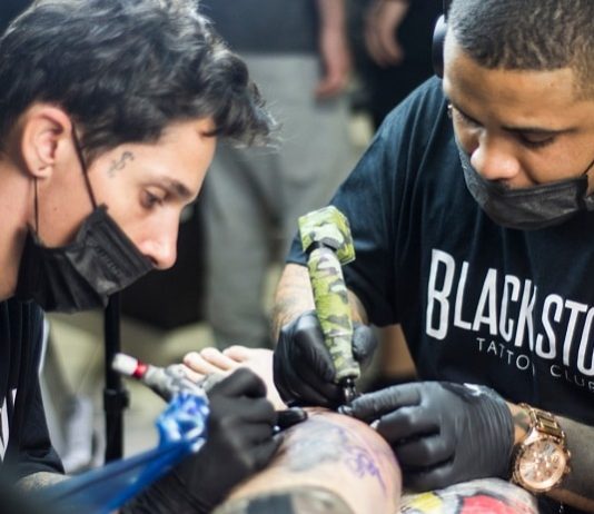 dois tatuadores usando máscara fazendo tatuagem em alguém