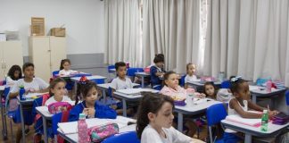crianças uniformizadas sentadas em carteiras de sala de aula
