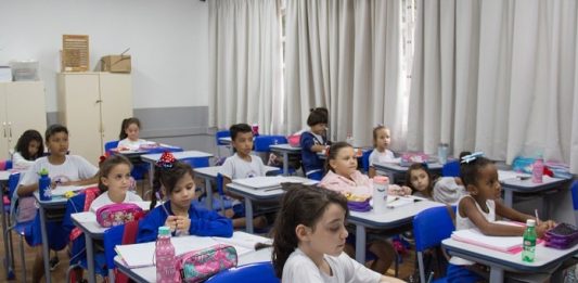 crianças uniformizadas sentadas em carteiras de sala de aula