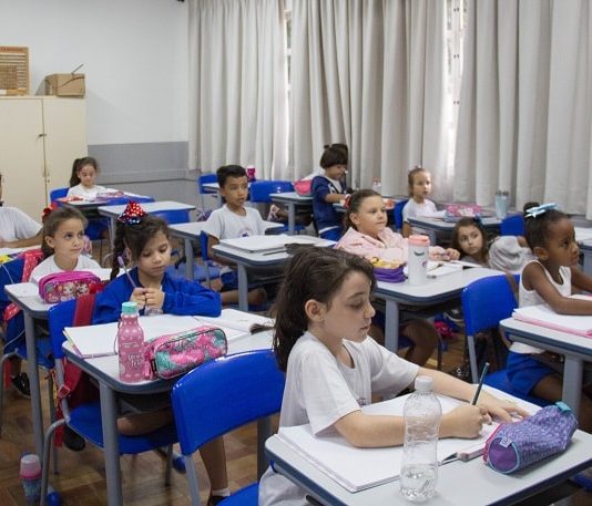 crianças uniformizadas sentadas em carteiras de sala de aula