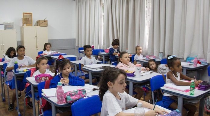 crianças uniformizadas sentadas em carteiras de sala de aula