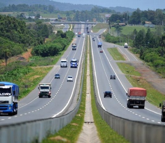 trecho da rodovia que se estende ao fundo da imagem com carros passando nos dois sentidos