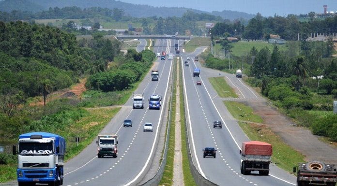 trecho da rodovia que se estende ao fundo da imagem com carros passando nos dois sentidos