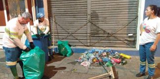um funcionário e duas funcionárias da comcap recolhem lixo de um calçadão em frente a comércio; homem fecha sacola de lixo