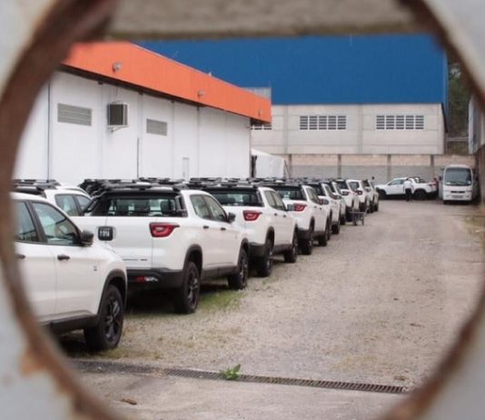 Secretaria de Educação explica a compra das caminhonetes fiat toro estacionadas juntas em pátio vistas por um buraco no portão