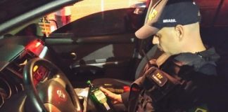 policial da prf sentado dentro de um carro da nissan segurando e olhando para uma garrafa de bebida alcoólica