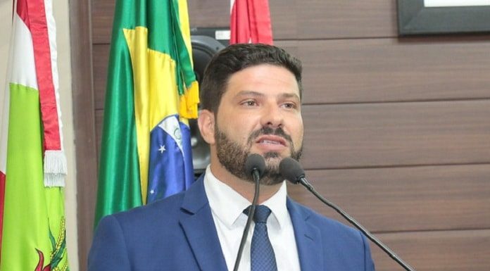 fábio braga fala na tribuna da câmara com bandeira de sc, brasil e florianópolis ao fundo