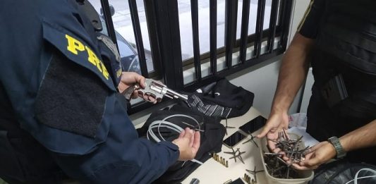mesa com os materiais apreendidos e um agente da prf e outro da gmsj ao lado mexendo nos objetos