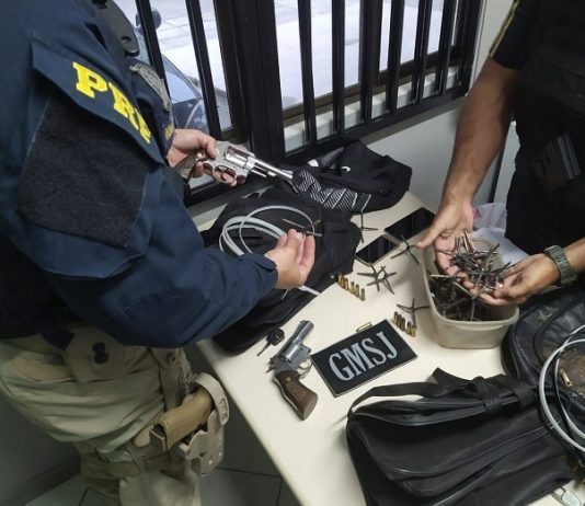 mesa com os materiais apreendidos e um agente da prf e outro da gmsj ao lado mexendo nos objetos