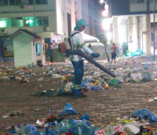 homem com uniforme da comcap e soprador limpa grande área cheia de lixo no centro