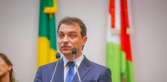 Moisés defende 1º ano de gestão e ouve vaias na Alesc a respeito da previdência moisés na tribuna da alesc falando ao microfone com bandeira do brasil e de sc ao fundo
