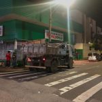 caminhão com entulhos estacionado em esquina com guarda em volta e em frente a uma farmácia popular