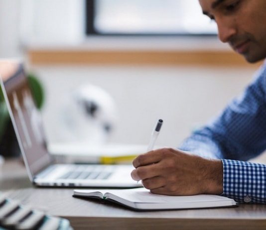 homem fazendo anotaçoes em um caderno ao lado de um notebook