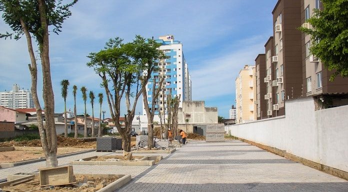 área com pavimento em paver do parque ao lado de longo muro e algumas árvores