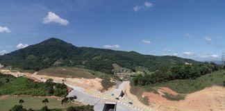 foto aérea de construção da rodovia onde há um túnel num pequeno morro