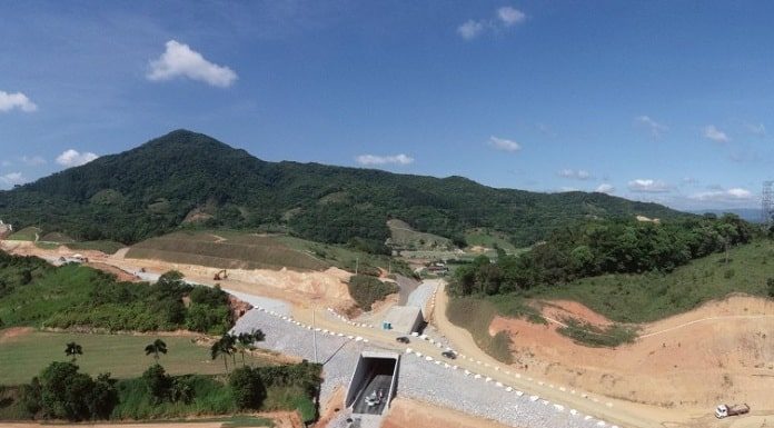 foto aérea de construção da rodovia onde há um túnel num pequeno morro