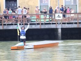 Equipe do IFSC de Florianópolis vence competição nacional de barcos solares O piloto Marcos comemora o término da prova, de pé no barco em frente ao um pier com pessoas