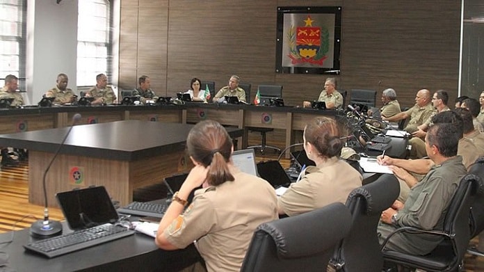 grande salão com bancada circular com policias militares (homens e mulheres) sentados em volta