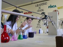 aluno e aluna mexem em ampolas e outros frascos de vidro com líquidos de diferentes cores em uma bancada