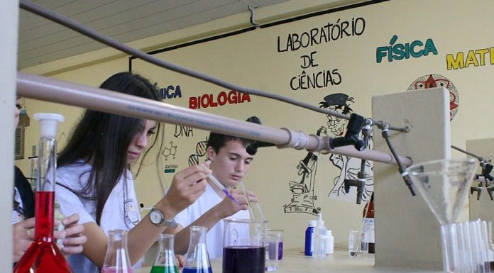 aluno e aluna mexem em ampolas e outros frascos de vidro com líquidos de diferentes cores em uma bancada