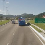 ônibus e carro passando pela via expressa sul e placa ao lado "rodovia aderbal ramos da silva"