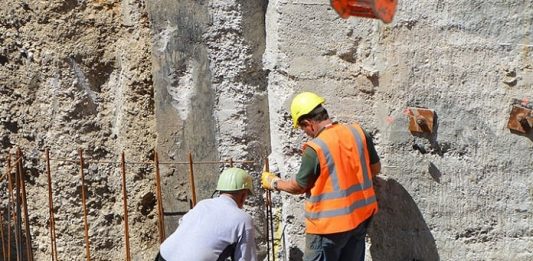Empregos em Santa Catarina: dois operários com equipamentos de proteção sobre estrutura de ferro dentro de grande buraco de obra