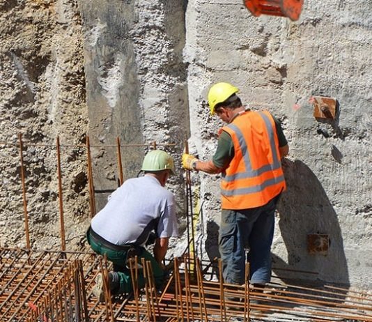 Empregos em Santa Catarina: dois operários com equipamentos de proteção sobre estrutura de ferro dentro de grande buraco de obra