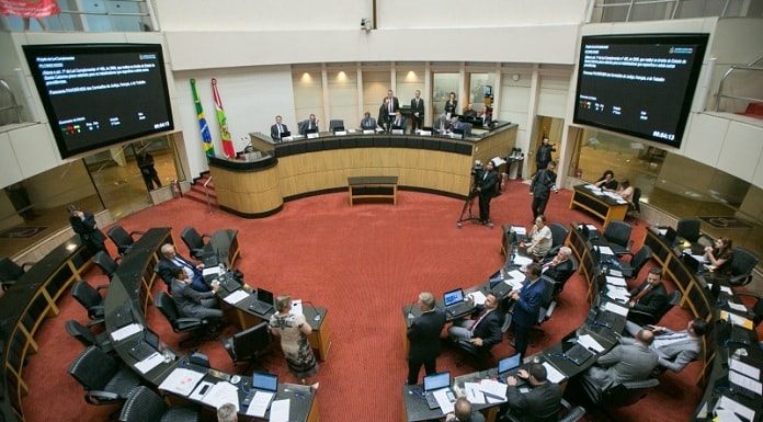 plenário da alesc visto de cima com as bancadas circulares ao centro e alguns deputados sentados