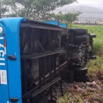 ônibus com número 11591 tombado de lado em terreno com mato