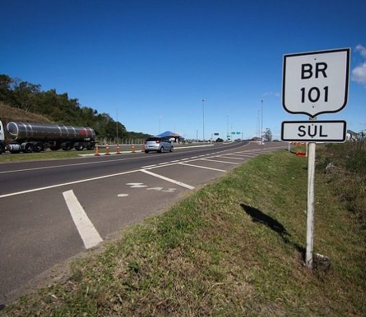 Concessionária tem vagas de emprego para atuar na BR 101 sul placa com inscrição br 101 sul ao lado da rodovia em dia de sol passando carros e caminhão