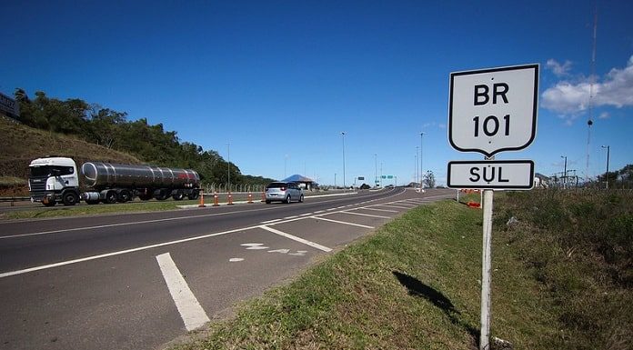 placa com inscrição br 101 sul ao lado da rodovia em dia de sol passando carros e caminhão