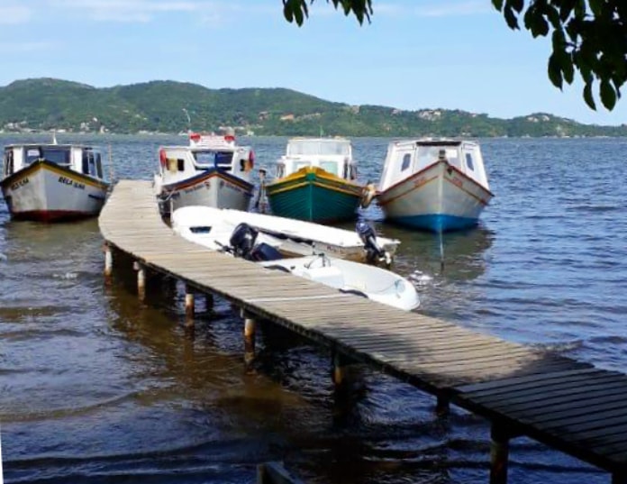 três barcos ancorados lado a lado junto ao final de um pier na lagoa e embarcação do outro lado